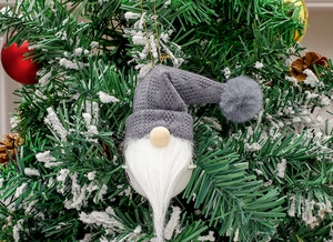 Close-up of a Nordic Christmas gnome bell ornament hanging on a snowy tree branch