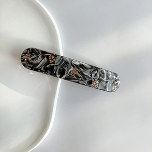 Detail of marble pattern hair clip with gold beads on white ceramic plate