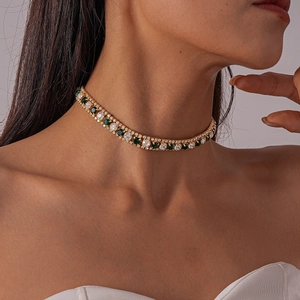 Detail of luxury gold choker necklace featuring alternating green and clear crystals on model
