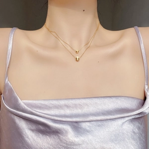 Double-layered gold chain necklace with polished oval bean pendants on female neck