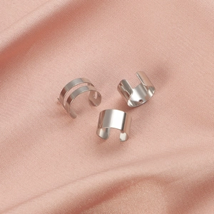 Three minimalist silver stainless steel ear cuffs on pink silk fabric professional display