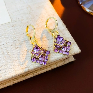 Macro shot of gold-plated leaf earrings with purple rhombic rhinestones on a linen book