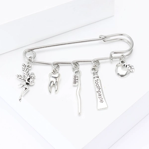 Silver alloy safety pin brooch with dental charms like tooth and brush on white background