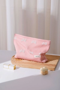Dettaglio della borsa trucco rosa con fiocco ricamato su un supporto in legno