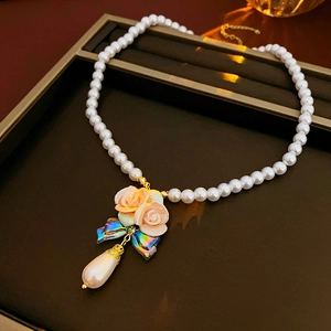 Macro detail of French floral necklace featuring pink rose bouquet and teardrop pearl