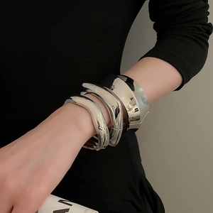 Close-up of three silver wavy bangles worn by a model in a high-fashion industrial design style