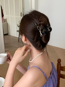 Rear view of model wearing a large black bow hair claw clip in a cozy home setting