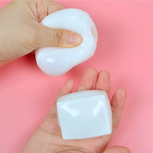 White cube squishy stress relief toy being squeezed on a soft pink background
