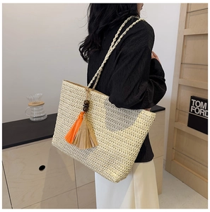 Detail of a large straw tote bag featuring colorful orange and brown tassels and wooden beads