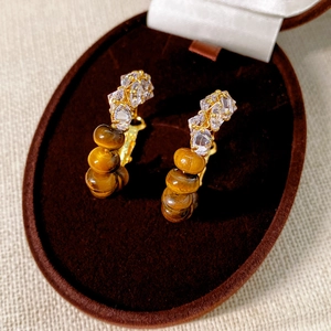 Macro detail of tiger eye stone earrings with crystals on a velvet display stand
