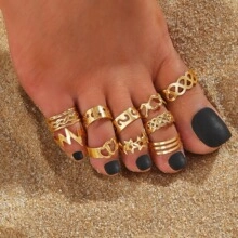 Close-up of 9 gold toe rings featuring heart and star designs on a beach setting