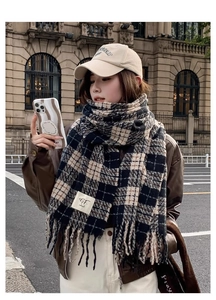 Detailed outdoor shot of a soft plaid scarf with tassels and a brand label detail