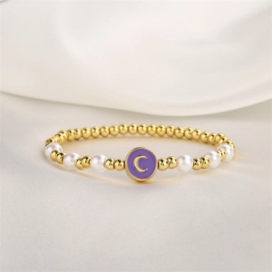 Détail macro d'un bracelet perlé avec billes dorées, perles et pendentif avec initiale C mauve