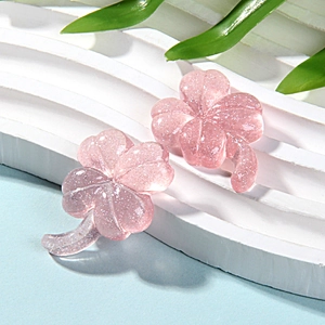 Macro view of pink glitter resin four-leaf clover stud earrings on a white leaf background