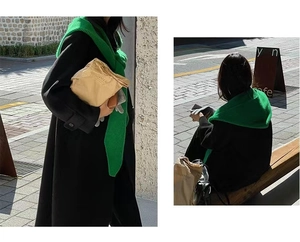 Detail shot of a casual green scarf shawl layered over a black coat in a cafe setting