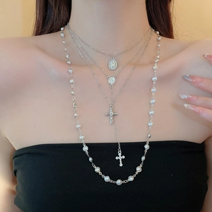 Detail of layered silver cross necklaces with pearl chain and religious pendants