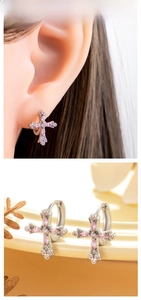Close-up of silver cross hoop earrings with pink zircon stones worn by a model