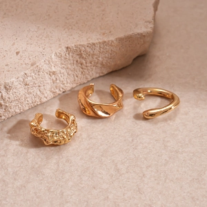 Detailed macro of three gold metal ear cuffs with irregular geometric and smooth designs