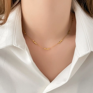 Close-up of golden beaded geometric necklace on a model wearing a white shirt