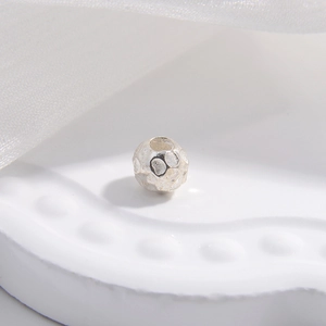 Macro detail of S925 sterling silver hammered bead with central hole on white tray