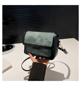 Detailed view of the dark green fabric texture and black leather trim on a flap bag