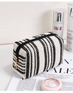 Detail of woven black and white striped makeup bag with gold zipper near beauty products