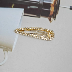 Golden teardrop hair clip with double row crystals on minimalist white background