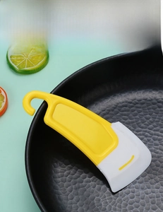 Close-up of yellow silicone scraper removing oil stains from a black textured cooking pan