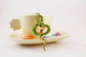 Close-up of a snake-shaped keychain with sparkling green rhinestones on a tea cup