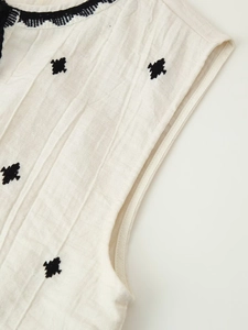 Detail of bohemian cream cotton vest showing textured fabric and black geometric embroidery