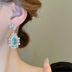 Close-up of blue teardrop pendant earrings with white pearls and zircon on model