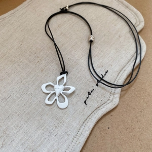 Detail showing white flower enamel pendant with heart engraving on a simple black cord