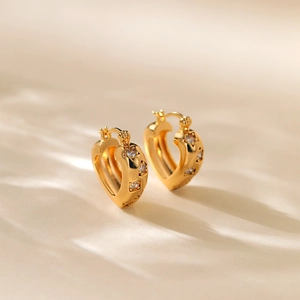 Elegant gold plated heart earrings with sparkling zircon stones on a beige surface