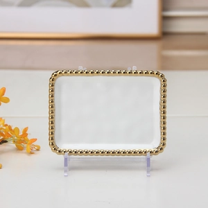 Close-up of a white rectangular ceramic plate with elegant gold beaded trim on the edge