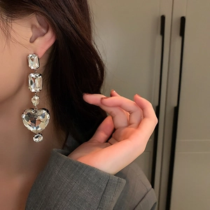 Close-up of dangling silver heart earrings with sparkling crystals worn by a model