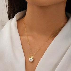 Close-up of a delicate gold bow necklace with a pearl pendant on a model's collarbone