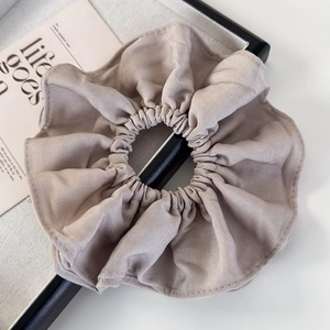 Detail of a large beige pleated fabric scrunchie on a tray with minimalist prop card