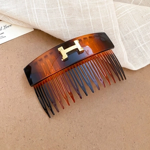 Close-up of tortoise shell resin hair comb featuring a gold H-shaped metallic emblem