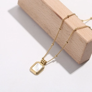 Elegant gold titanium square shell pendant necklace hanging on minimalist wood block