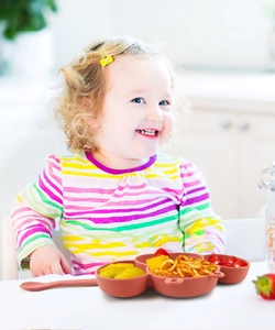 Toddler using multi-compartment silicone suction plate and spoon set during mealtime