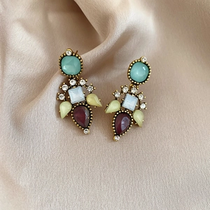 Detail of vintage gold earrings with multi-colored gemstones on champagne satin background