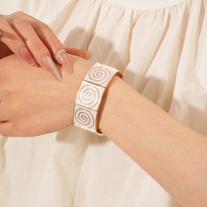 Detailed close-up of a vintage gold-tone wide bracelet with white enamel spiral patterns