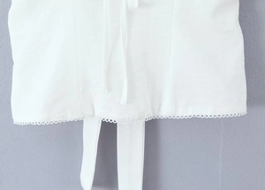 Détail de gilet blanc avec dentelle ondulée évidée et design de nœud à l'ourlet