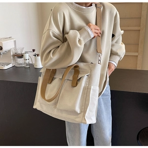 Detailed view of cream canvas tote bag with front pockets and brown shoulder straps