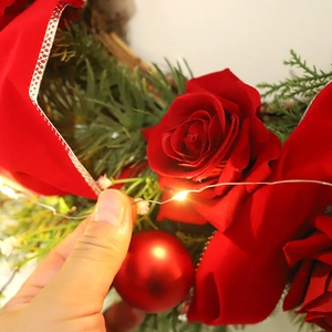 Christmas wreath with red roses, green pine needles, and warm LED fairy lights decoration