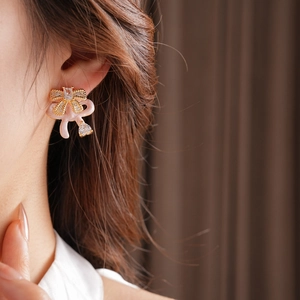 Side view detail of a pink bow earring with crystals worn by a model in soft lighting