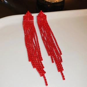 Close-up of red rhinestone tassel earrings on a ceramic tray with sparkling detail