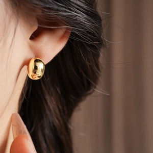 Close-up of minimalist gold plated oval earrings showing polished mirror finish on earlobe