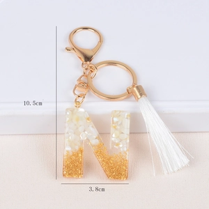Detailed view of resin letter N keychain with gold foil flakes and white silk tassel