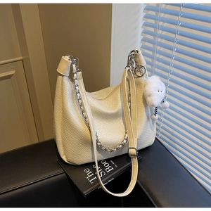 Detail view of cream woven shoulder bag with cloud charm on a book in a lifestyle setting